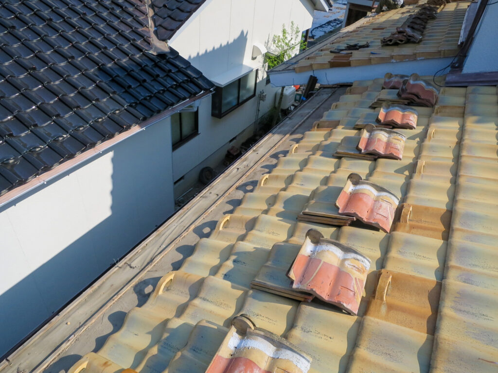 先端瓦を2枚ほどめくって吊り金物にアクセスしている様子